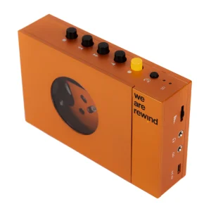 Orange rectangular portable audio device with five black knobs and one yellow knob on top, a circular window on the side, and the "we are rewind" branding.