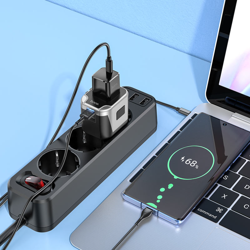 Hoco. Ac5 Dual Usb Universal Charger Adapter A hoco. Ac5 dual usb universal charger adapter with multiple devices plugged in, including chargers, a phone displaying a 68% charge, and a laptop on a blue surface.